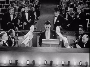 Movie still from “The Broadway Melody” (1929), directed by Harry Beaumont – A man sitting at a table in front of a crowd; Wide shot, High angle