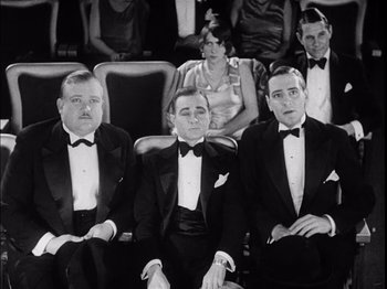 Movie still from “The Broadway Melody” (1929), directed by Harry Beaumont – A group of men sitting next to each other in tuxedos; Medium shot, Low angle