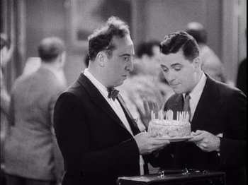 Movie still from “The Broadway Melody” (1929), directed by Harry Beaumont – Two men in suits and ties holding a cake; Medium shot, High angle