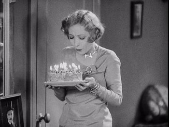 Movie still from “The Broadway Melody” (1929), directed by Harry Beaumont – A black and white photo of a woman holding a birthday cake; Medium shot, High angle