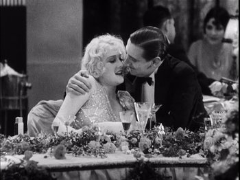 Movie still from “The Broadway Melody” (1929), directed by Harry Beaumont – A man and a woman sitting at a table kissing; Medium shot, High angle