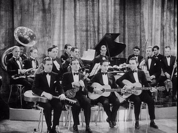 Movie still from “The Broadway Melody” (1929), directed by Harry Beaumont – A group of men in tuxedos holding instruments; Wide shot, High angle