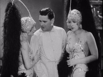 Movie still from “The Broadway Melody” (1929), directed by Harry Beaumont – A man standing next to two showgirls in costume; Medium shot, Low angle