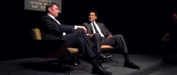 Movie still from “Ali” (2001), directed by Michael Mann – A couple of men sitting on top of a couch; Medium shot, Over the shoulder angle