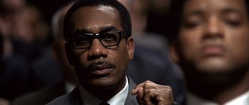 Movie still from “Ali” (2001), directed by Michael Mann – A person wearing a suit and glasses; Close Up shot, Low angle
