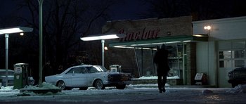 Movie still from “Ali” (2001), directed by Michael Mann – A man walking down the street in front of a gas station at night; Extreme Wide shot, Over the shoulder angle