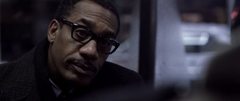 Movie still from “Ali” (2001), directed by Michael Mann – A person wearing a suit and glasses; Close Up shot, Over the shoulder angle