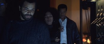 Movie still from “Ali” (2001), directed by Michael Mann – Two men and a woman standing next to each other in a dark room; Medium shot, Low angle