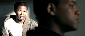 Movie still from “Ali” (2001), directed by Michael Mann – A man in a brown and white checkered sweater; Close Up shot, Over the shoulder angle