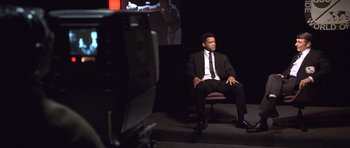 Movie still from “Ali” (2001), directed by Michael Mann – A man sitting in a chair in front of a television; Medium shot, Over the shoulder angle