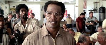 Movie still from “Ali” (2001), directed by Michael Mann – A person wearing glasses with other people in the background; Close Up shot, High angle