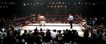 Movie still from “Ali” (2001), directed by Michael Mann – A boxing match in a boxing ring with people watching; Extreme Wide shot, High angle