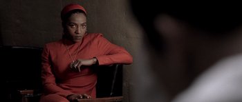 Movie still from “Ali” (2001), directed by Michael Mann – A woman sitting in a chair wearing a red dress; Close Up shot, Over the shoulder angle