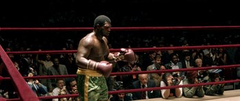Movie still from “Ali” (2001), directed by Michael Mann – A man wearing boxing gloves in a boxing ring with people watching; Medium shot, High angle