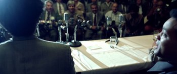 Movie still from “Ali” (2001), directed by Michael Mann – A group of people sitting around a table with microphones; Extreme Close Up shot, Over the shoulder angle
