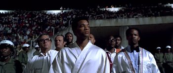 Movie still from “Ali” (2001), directed by Michael Mann – A group of men standing next to each other in a stadium; Medium shot, Low angle