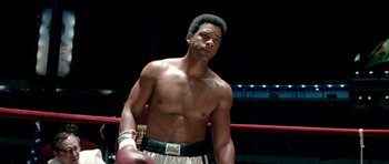 Movie still from “Ali” (2001), directed by Michael Mann – A man standing in a boxing ring with his hands on his hips; Medium shot, Low angle