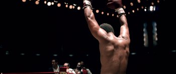 Movie still from “Ali” (2001), directed by Michael Mann – A man is raising his hands in a boxing ring; Medium shot, Low angle