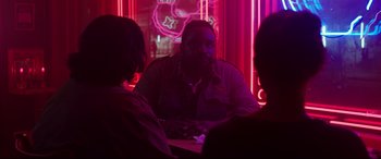Movie still from “Godzilla vs. Kong” (2021), directed by Adam Wingard – Three people sitting at a table in front of a neon sign; Medium shot, Over the shoulder angle