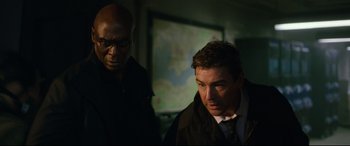 Movie still from “Godzilla vs. Kong” (2021), directed by Adam Wingard – Two men standing next to each other in front of a map; Medium shot, Over the shoulder angle