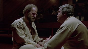 Movie still from “The Brood” (1979), directed by David Cronenberg – Two men are sitting in a room and one of them has his hands on another man's hand; Medium shot, High angle