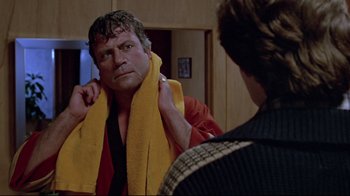 Movie still from “The Brood” (1979), directed by David Cronenberg – A man with a towel around his neck is looking at himself in the mirror; Close Up shot, Over the shoulder angle