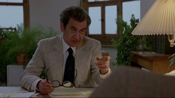 Movie still from “The Brood” (1979), directed by David Cronenberg – A man sitting at a table holding a piece of paper in front of him; Medium shot, Over the shoulder angle