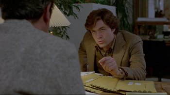 Movie still from “The Brood” (1979), directed by David Cronenberg – A man sitting at a table talking to another man; Medium shot, Over the shoulder angle