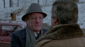 Movie still from “The Brood” (1979), directed by David Cronenberg – An older man wearing a hat talking to another older man; Close Up shot, Over the shoulder angle