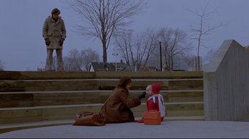 Movie still from “The Brood” (1979), directed by David Cronenberg – A woman sitting on the ground next to a child; Wide shot, High angle