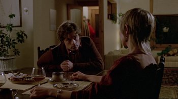 Movie still from “The Brood” (1979), directed by David Cronenberg – Two people sitting at a dinner table talking to each other; Medium shot, Over the shoulder angle