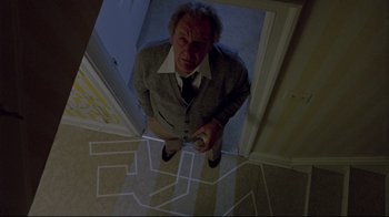 Movie still from “The Brood” (1979), directed by David Cronenberg – A man standing in a room with a remote control in his hand; Wide shot, Overhead angle