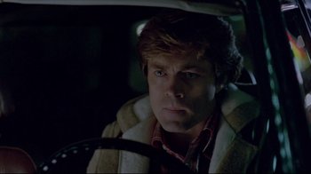Movie still from “The Brood” (1979), directed by David Cronenberg – A man in a brown jacket sitting in a car at night; Close Up shot, Over the shoulder angle