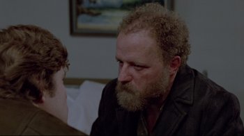 Movie still from “The Brood” (1979), directed by David Cronenberg – A man with a long beard sitting next to a woman; Close Up shot, Over the shoulder angle