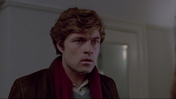 Movie still from “The Brood” (1979), directed by David Cronenberg – A man with long brown hair wearing a brown jacket and a red scarf; Close Up shot, Over the shoulder angle