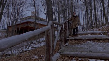 Movie still from “The Brood” (1979), directed by David Cronenberg – A man in a brown coat standing next to a wooden fence; Wide shot, Low angle