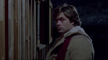 Movie still from “The Brood” (1979), directed by David Cronenberg – A man wearing a coat and scarf standing in front of a wooden fence; Close Up shot, Over the shoulder angle