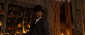 Movie still from “The Brothers Bloom” (2008), directed by Rian Johnson – A man wearing a suit and hat in a dimly - lit room; Medium shot, Low angle