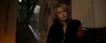 Movie still from “The Brothers Bloom” (2008), directed by Rian Johnson – A woman in a black jacket standing in front of a staircase; Close Up shot, Low angle