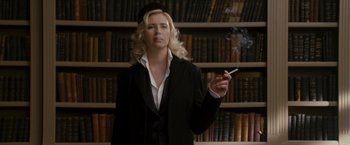 Movie still from “The Brothers Bloom” (2008), directed by Rian Johnson – A woman smoking a cigarette in front of bookshelves; Medium shot, Low angle