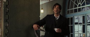 Movie still from “The Brothers Bloom” (2008), directed by Rian Johnson – A man in a suit and tie holding a coffee cup; Medium shot, Over the shoulder angle