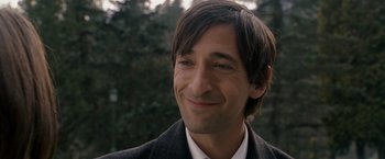Movie still from “The Brothers Bloom” (2008), directed by Rian Johnson – A person wearing a suit and smiling; Close Up shot, Over the shoulder angle