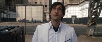 Movie still from “The Brothers Bloom” (2008), directed by Rian Johnson – A man in a white suit standing in front of a building; Close Up shot, Over the shoulder angle