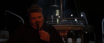 Movie still from “The Brothers Bloom” (2008), directed by Rian Johnson – A man smoking a cigarette in front of a boat; Medium shot, Over the shoulder angle