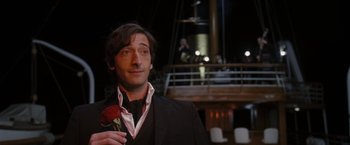 Movie still from “The Brothers Bloom” (2008), directed by Rian Johnson – A man holding a red rose while wearing a suit and tie; Medium shot, Over the shoulder angle