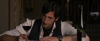 Movie still from “The Brothers Bloom” (2008), directed by Rian Johnson – A person sitting at a table with a glass of wine; Close Up shot, Over the shoulder angle