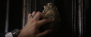 Movie still from “The Brothers Bloom” (2008), directed by Rian Johnson – A hand is touching a door knob on a wooden door; Extreme Close Up shot, High angle