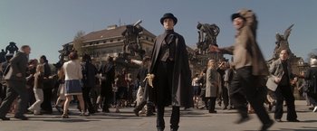 Movie still from “The Brothers Bloom” (2008), directed by Rian Johnson – A man in a black hat and a black coat is standing in front of a group of people; Wide shot, Low angle