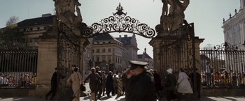 Movie still from “The Brothers Bloom” (2008), directed by Rian Johnson – A crowd of people walking on a street under an ornate arch; Extreme Wide shot, High angle