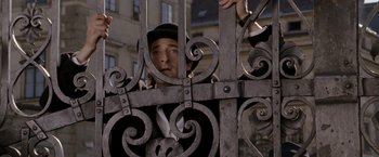 Movie still from “The Brothers Bloom” (2008), directed by Rian Johnson – A man is looking through a metal gate; Medium shot, Low angle